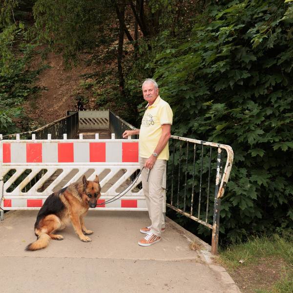 Ein Mann und ein Hund stehen vor dem gesperrten Zugang zu einer Brücke.