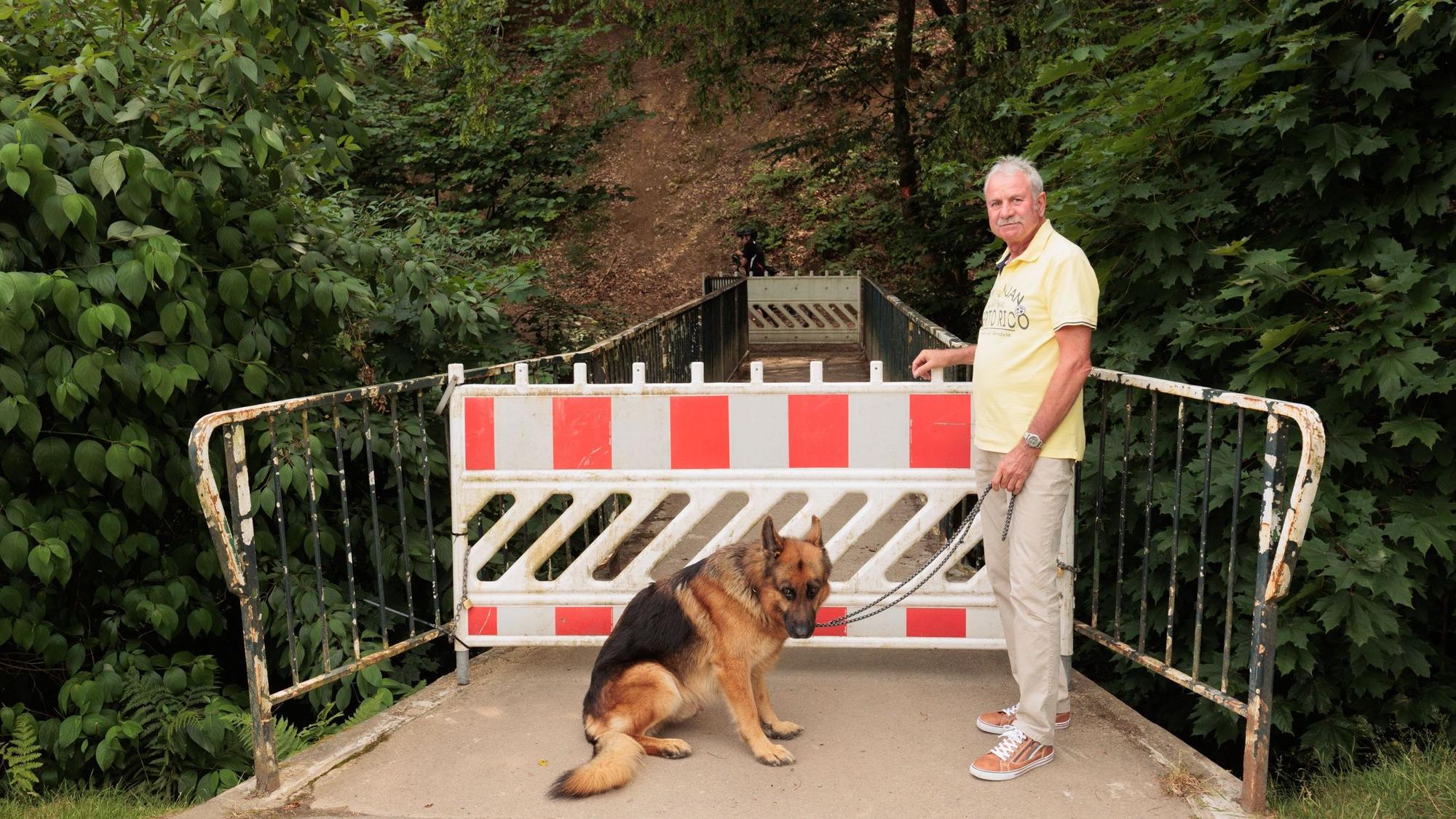 Ein Mann und ein Hund stehen vor dem gesperrten Zugang zu einer Brücke.