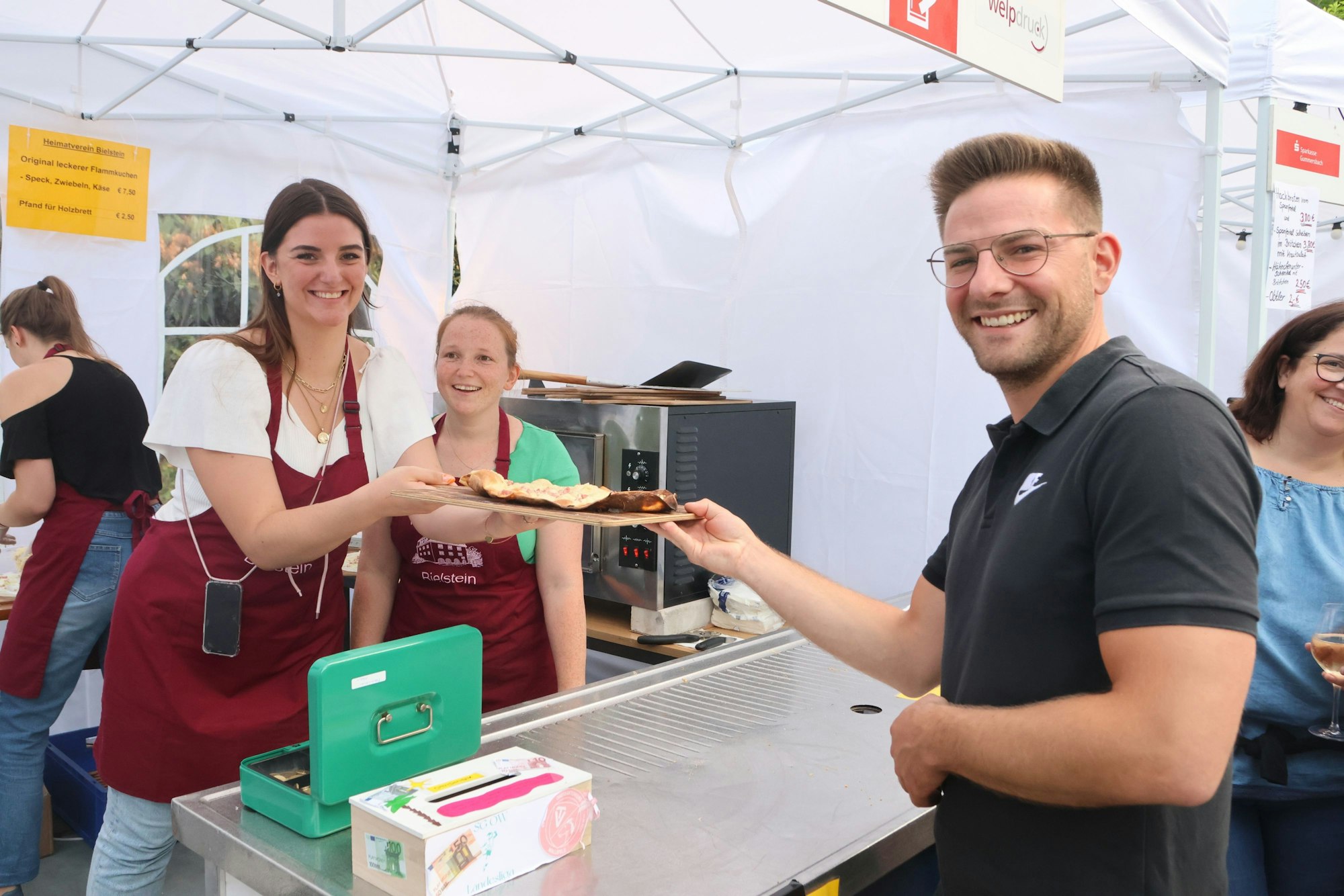 Jannick Binner kauft Flammkuchen bei Zoi Andrieu (links) und Anni Hartmann.