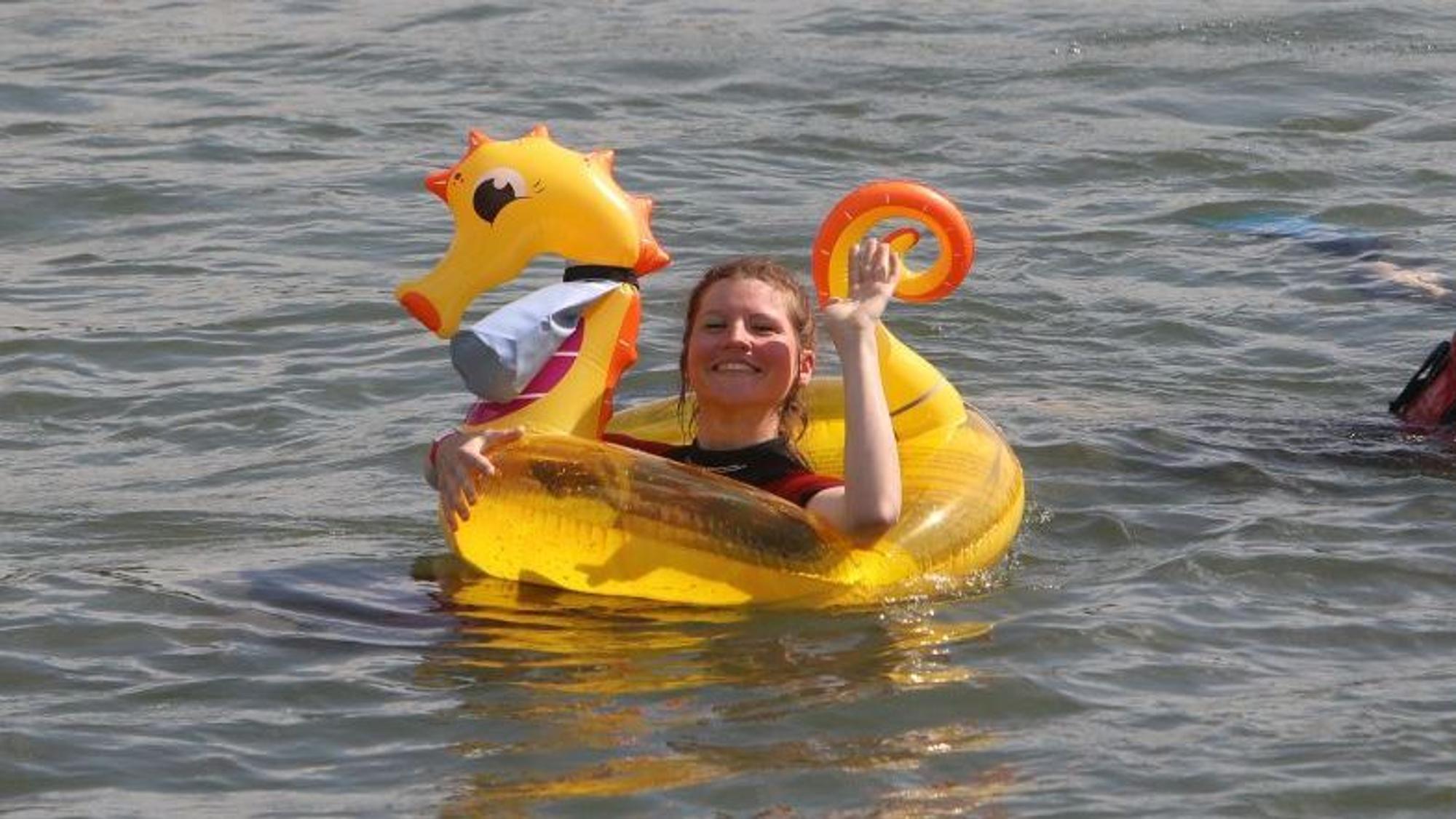 Eins Schwimmerin mit einem gelben Drachen winkt in die Kamera.