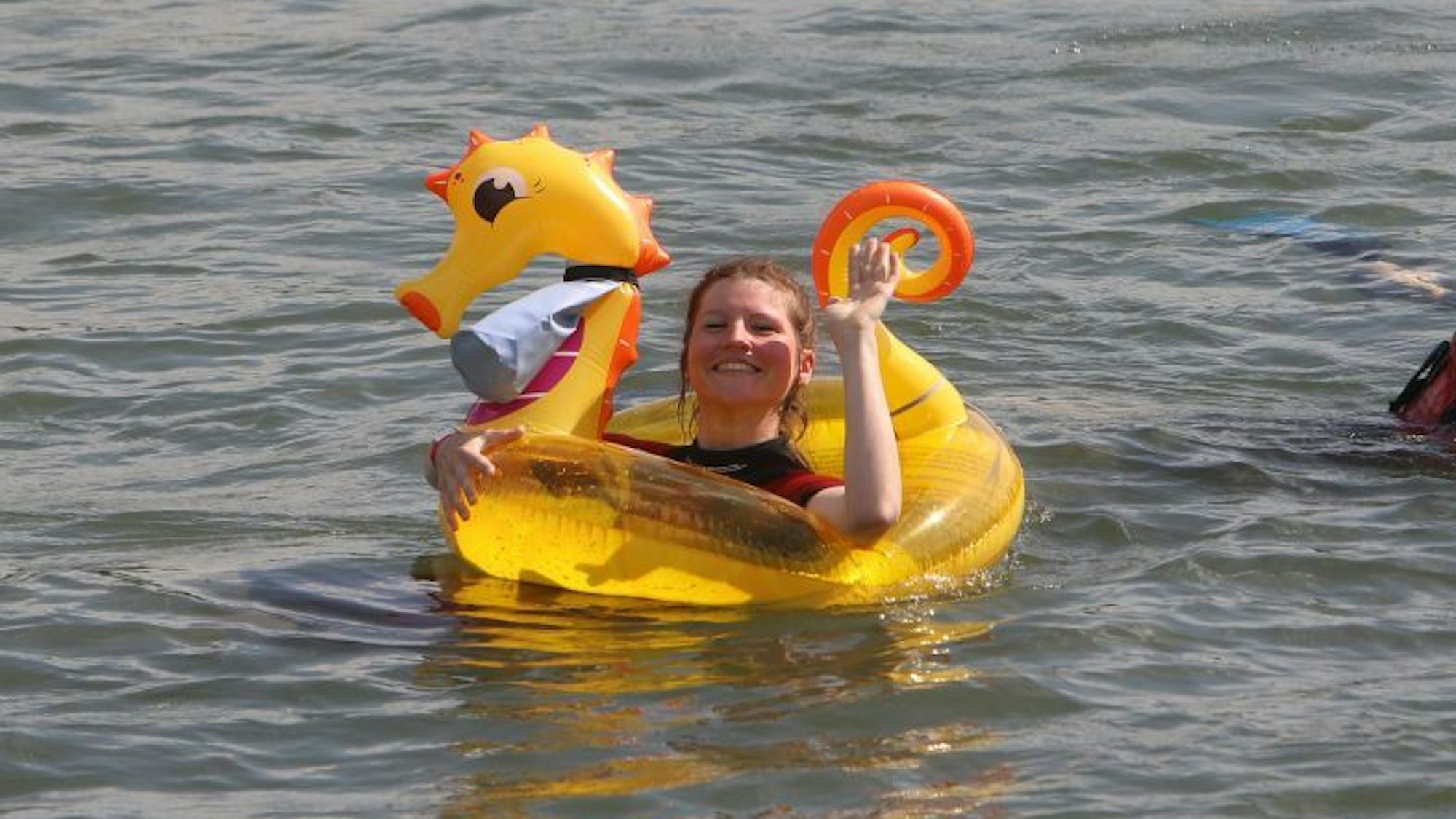 Eins Schwimmerin mit einem gelben Drachen winkt in die Kamera.