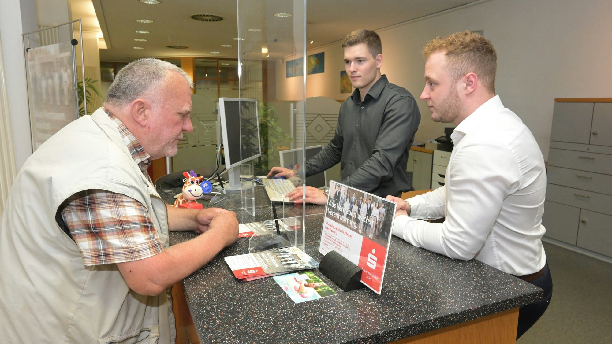 Malte Schnell (M.), Leiter der „Azubi-Filiale“, und Alexander Görlach (r.) betreuen einen Kunden.