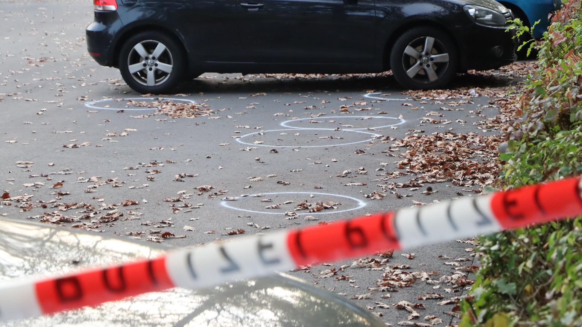 Das Bild zeigt einen Parkplatz mit Fahrzeugen. Davor lieben Patronenhülsen, die mit weißer Kreide eingekreist sind.