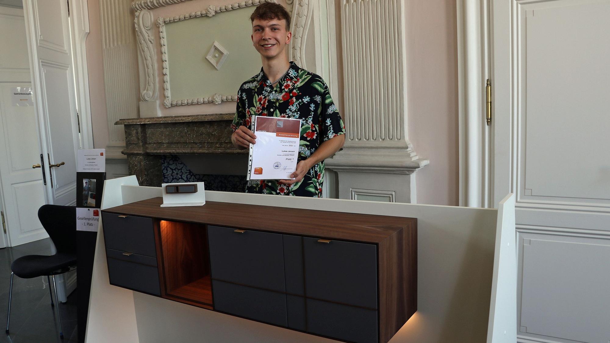 Das Bild zeigt Lukas Jensen aus Frechen an seinem Gesellenstück, einem beleuchteten Sideboard.