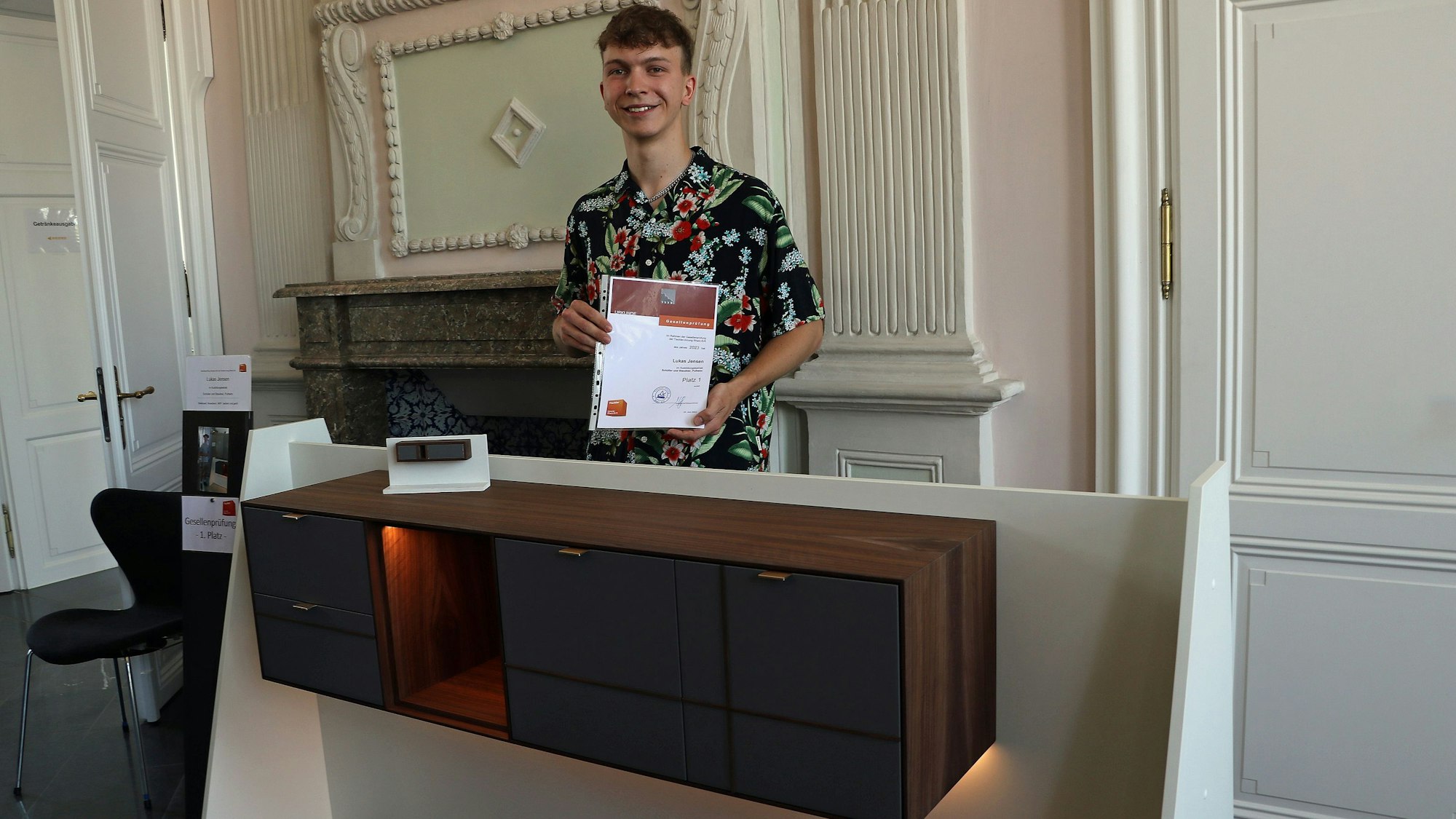 Das Bild zeigt Lukas Jensen aus Frechen an seinem Gesellenstück, einem beleuchteten Sideboard.