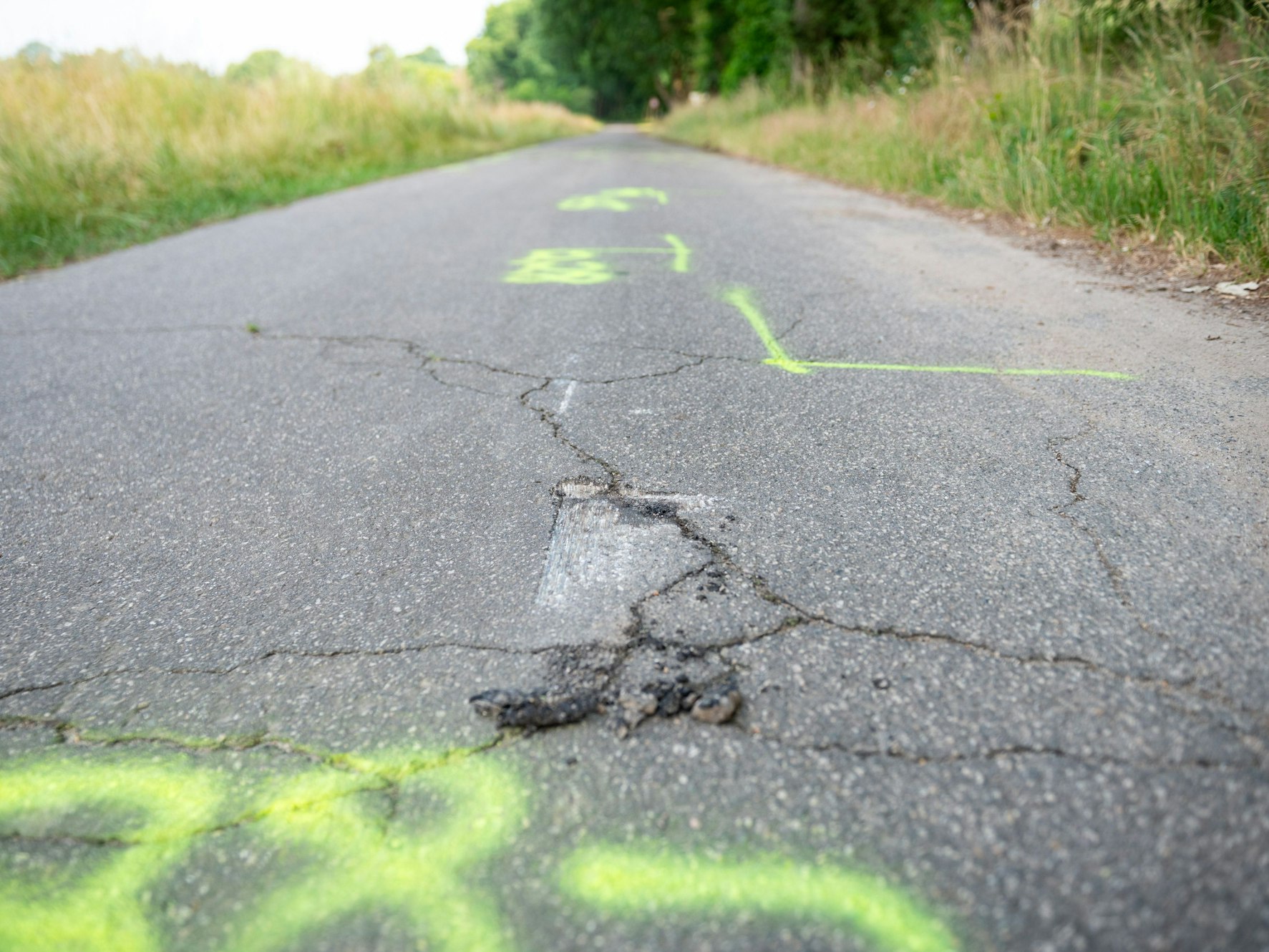 Gelbe Markierungen der Polizei und ein Schaden an der Fahrbahn auf der Straße am Unfallort.