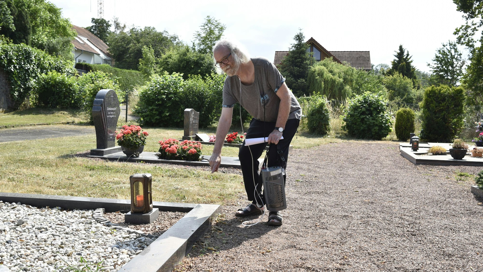 Ein älterer Mann deutet auf ein Grab auf einem Friedhof.