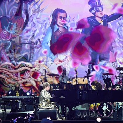 Elton John bei seiner Bühnenshow auf dem Glastonbury-Festival. Die Bühne ist bunt und farbenfroh.