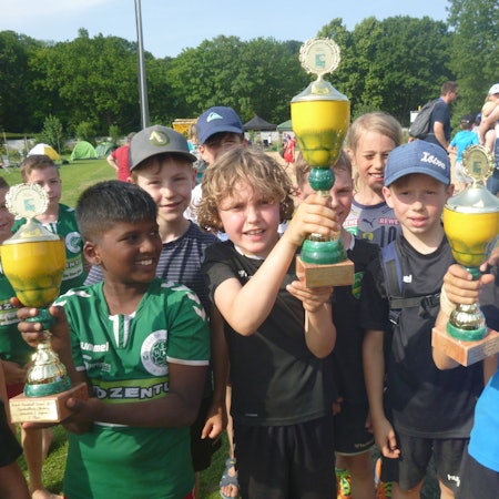 Kinder präsentieren stolz drei Pokale.
