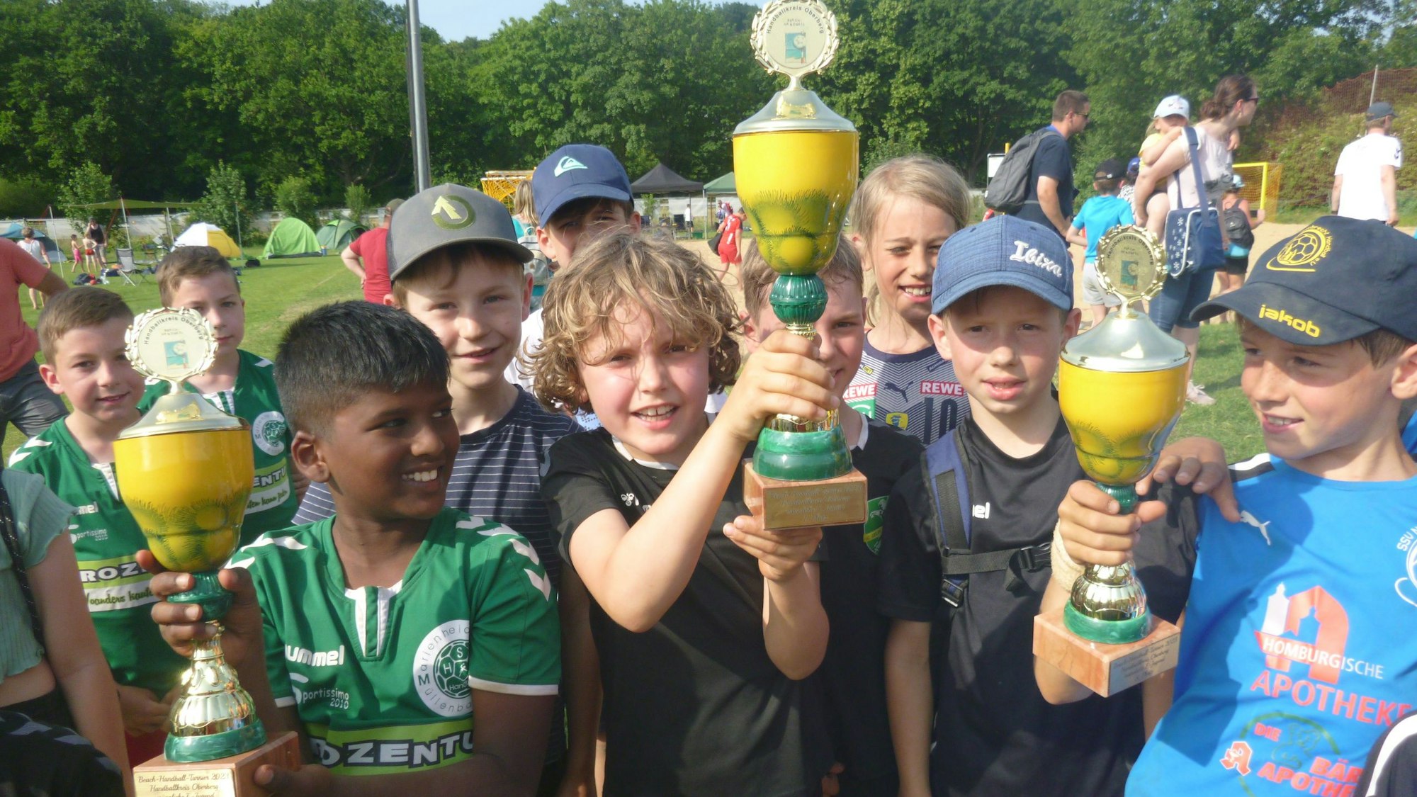 Kinder präsentieren stolz drei Pokale.