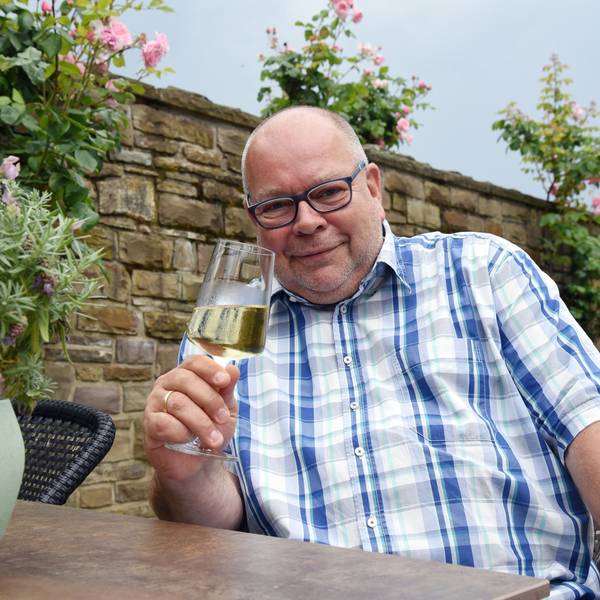 Ein Mann im karierten Hemd hält ein Glas Weißwein in der Hand.