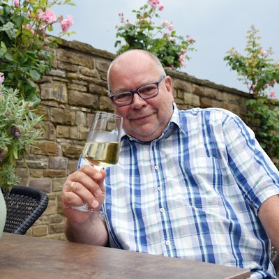 Ein Mann im karierten Hemd hält ein Glas Weißwein in der Hand.