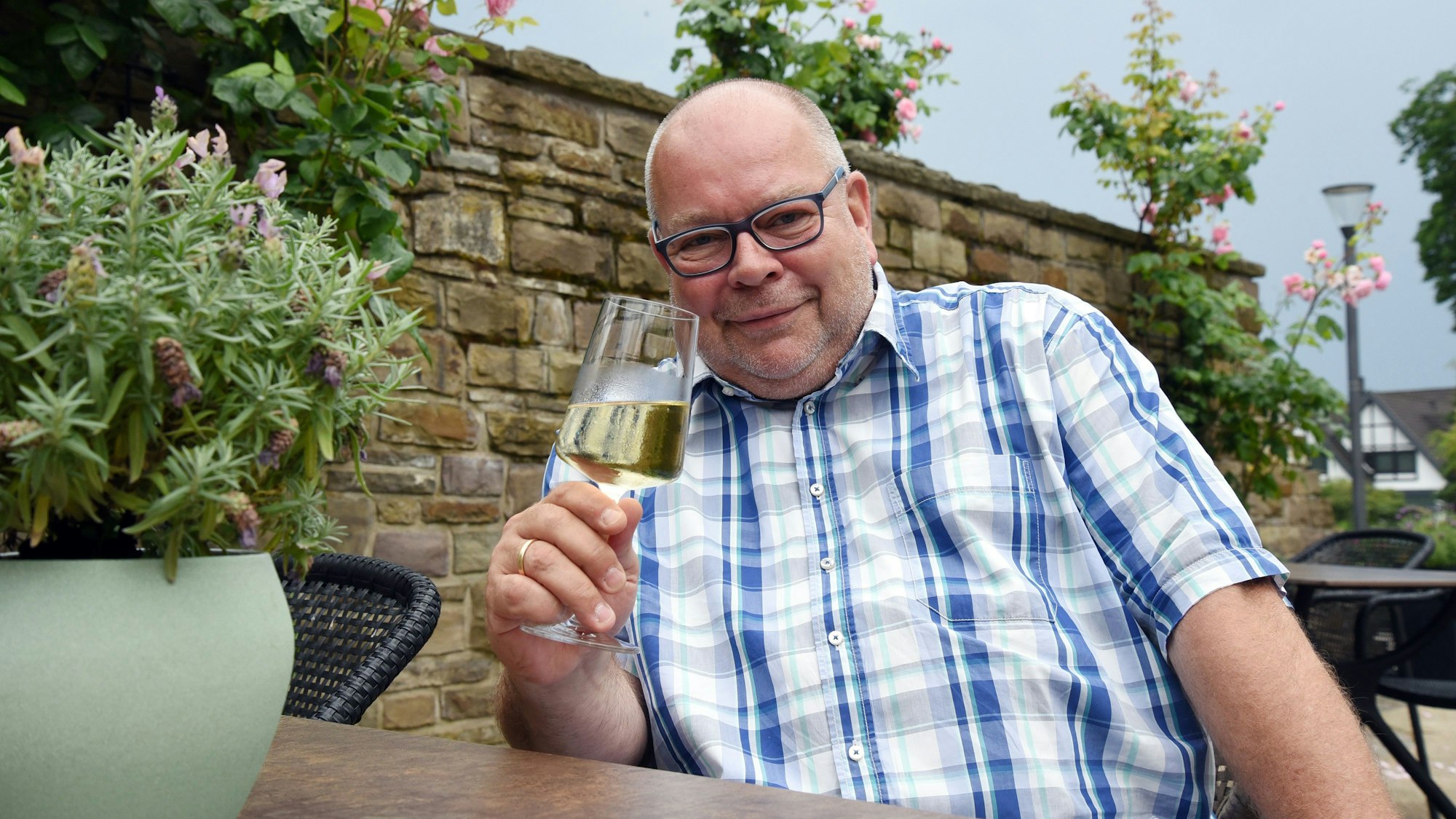 Ein Mann im karierten Hemd hält ein Glas Weißwein in der Hand.