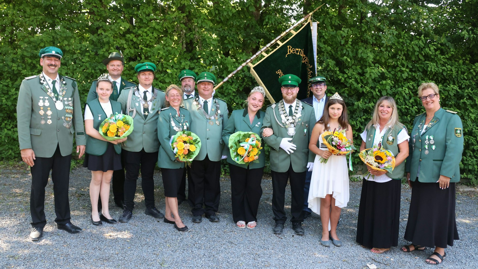 Mehrere Erwachsene und Kinder stehen in einer Reihe nebeneinander. Sie tragen Schützenuniformen und Kleider.