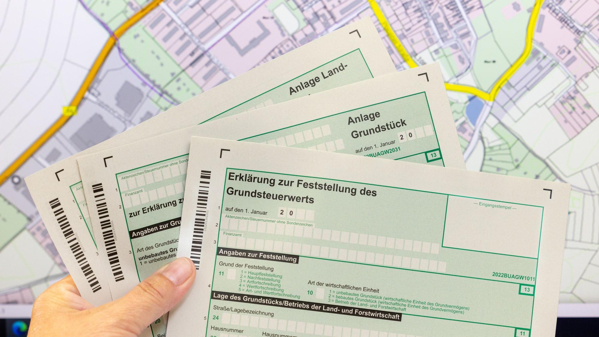 Eine Mitarbeiterin hält im Finanzamt Formulare zur Grundsteuererklärung in der Hand.