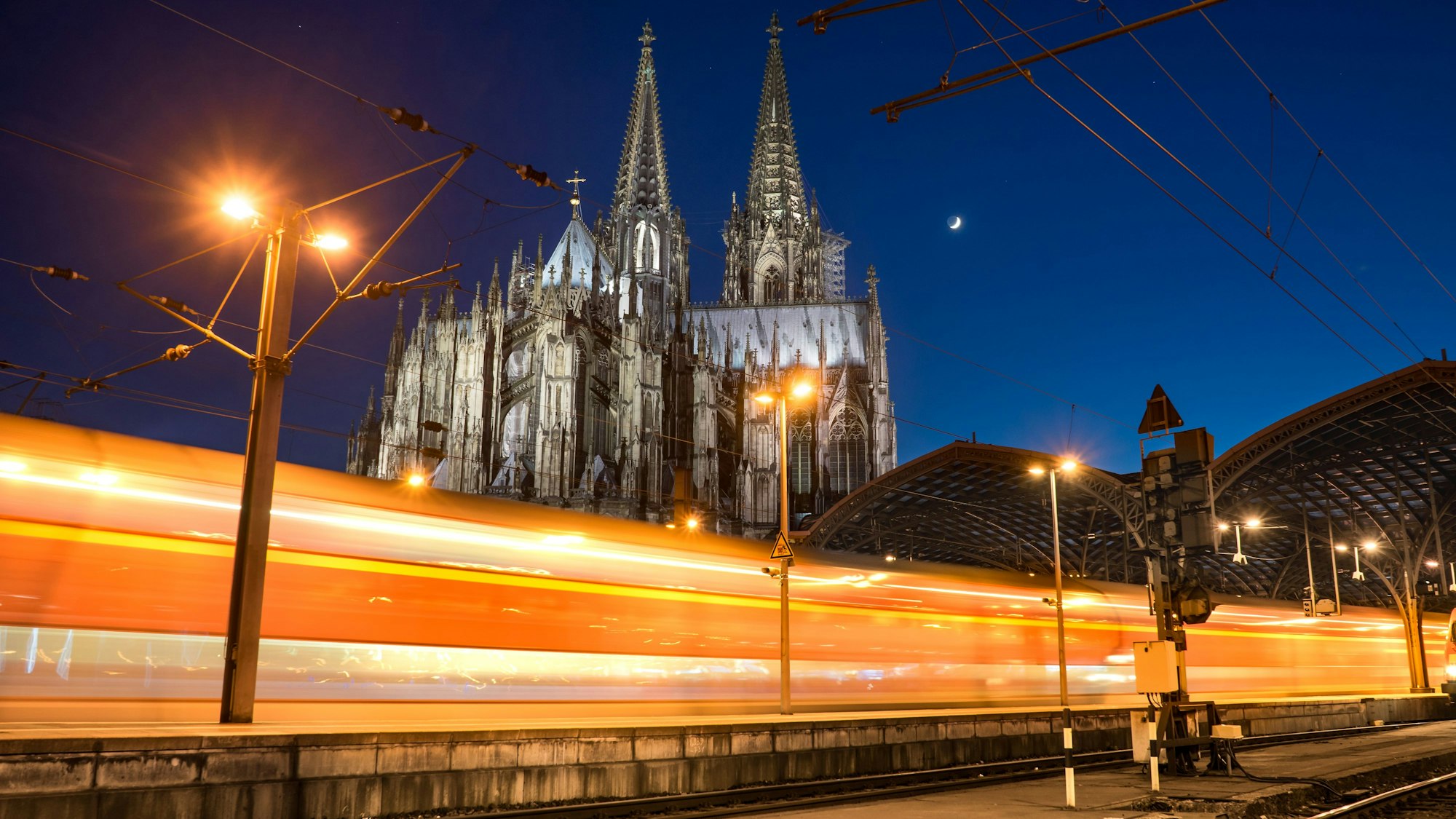 Ein Zug fährt im Dunkeln am Kölner Dom vorbei.