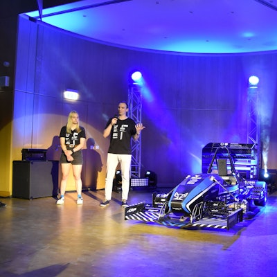 Rollout des neuen Rennwagens der Hochschule Bonn-Rhein-Sieg: Experten erklären die neu entwickelten Bauteile. Drei Männer und eine Frau stehen neben dem Rennwagen auf der Bühne.