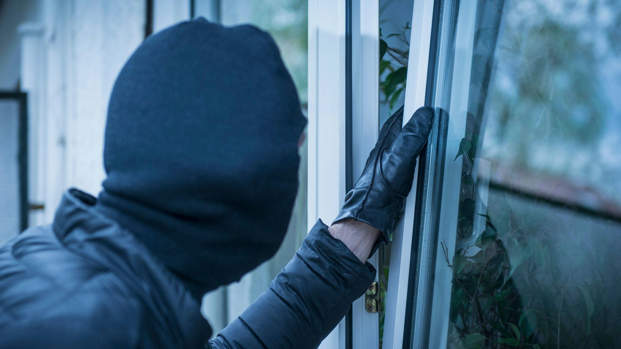 Ein maskierter Einbrecher versucht, ein Fenster zu öffnen.