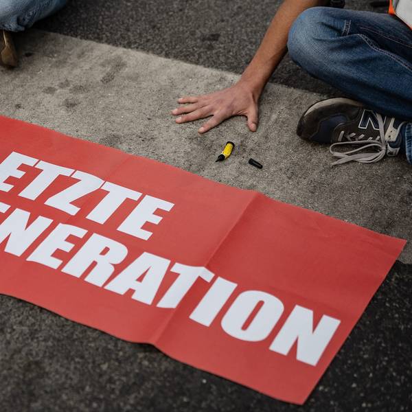 Ein Aktivist der Gruppe Letzte Generation, der seine Hand auf der Straße festgeklebt hat, blockiert eine Kreuzung.