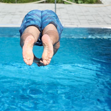 Ein Mann springt von einem Sprungbrett kopfüber ins Wasser.