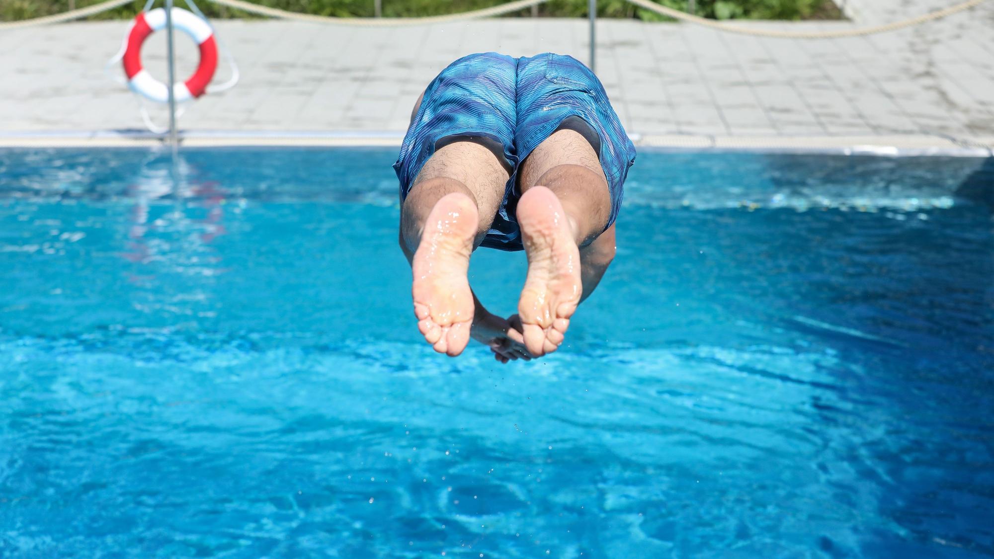 Ein Mann springt in ein Schwimmbecken in einem Freibad, im Hintergrund ist ein Rettungsring zu sehen. (Symbolbild)