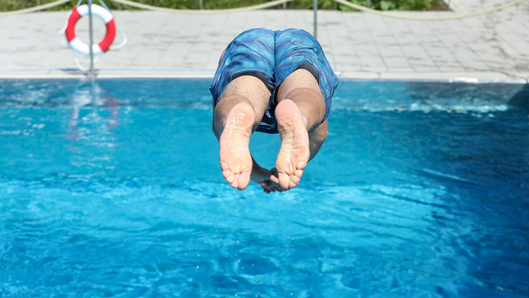 Ein Mann springt in ein Schwimmbecken in einem Freibad, im Hintergrund ist ein Rettungsring zu sehen. (Symbolbild)