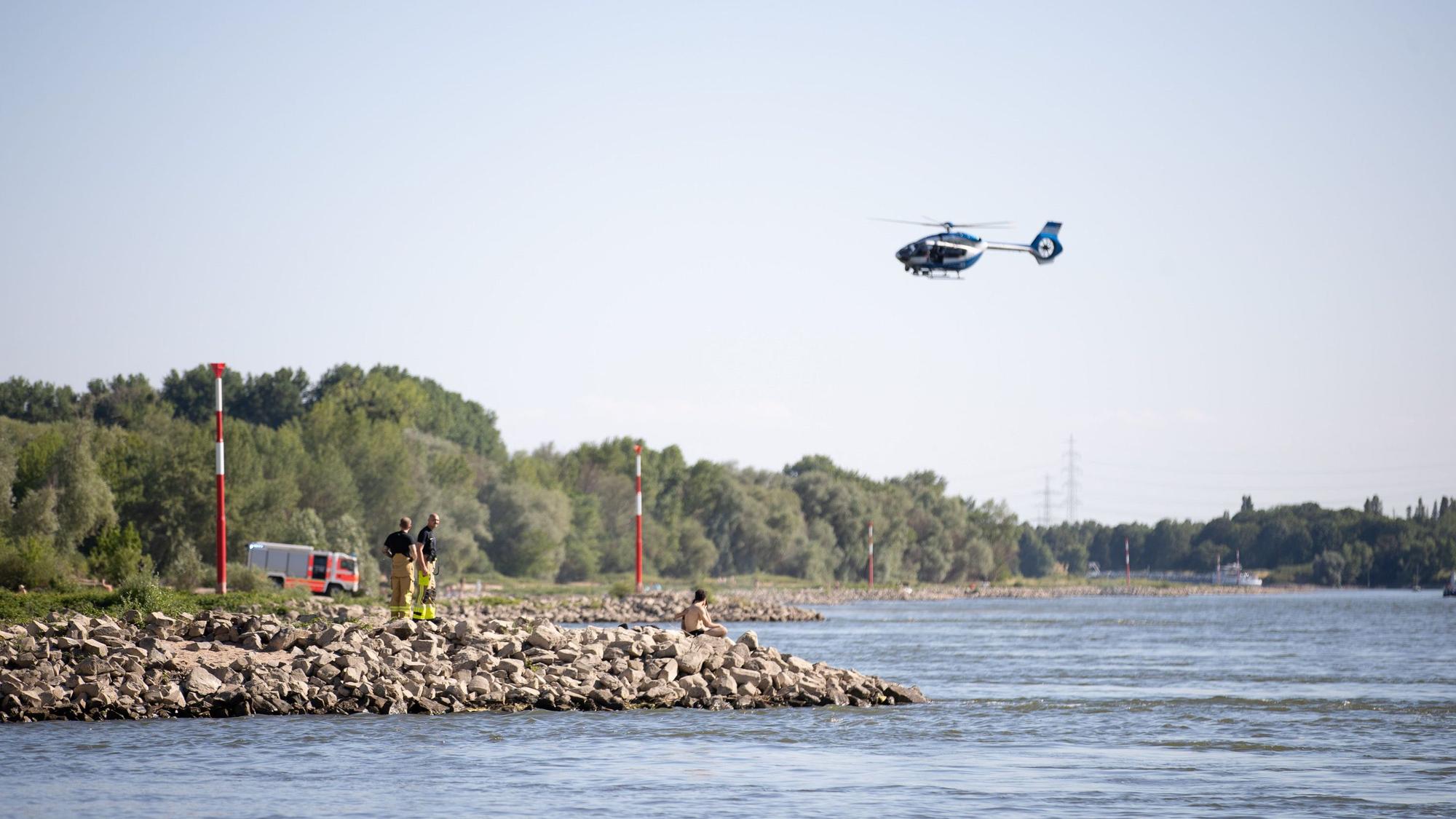 Aus einem Hubschrauber und vom Ufer aus suchen Einsatzkräfte nach einem Schwimmer, der im Rheim von einem Sog erfasst und mitgerissen wurde.