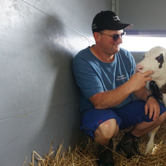 Landwirt Sebastian Bützler kniet neben einem Kalb.