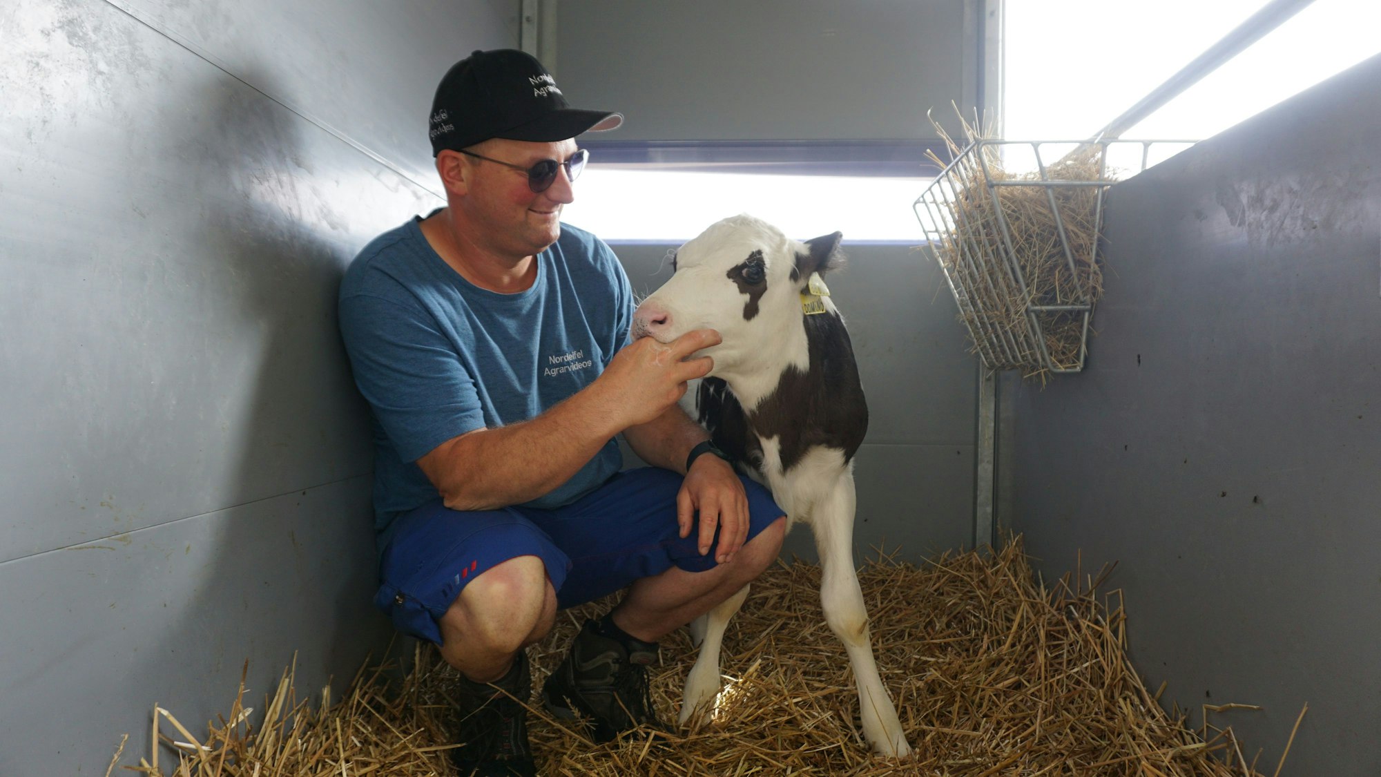 Landwirt Sebastian Bützler kniet neben einem Kalb.
