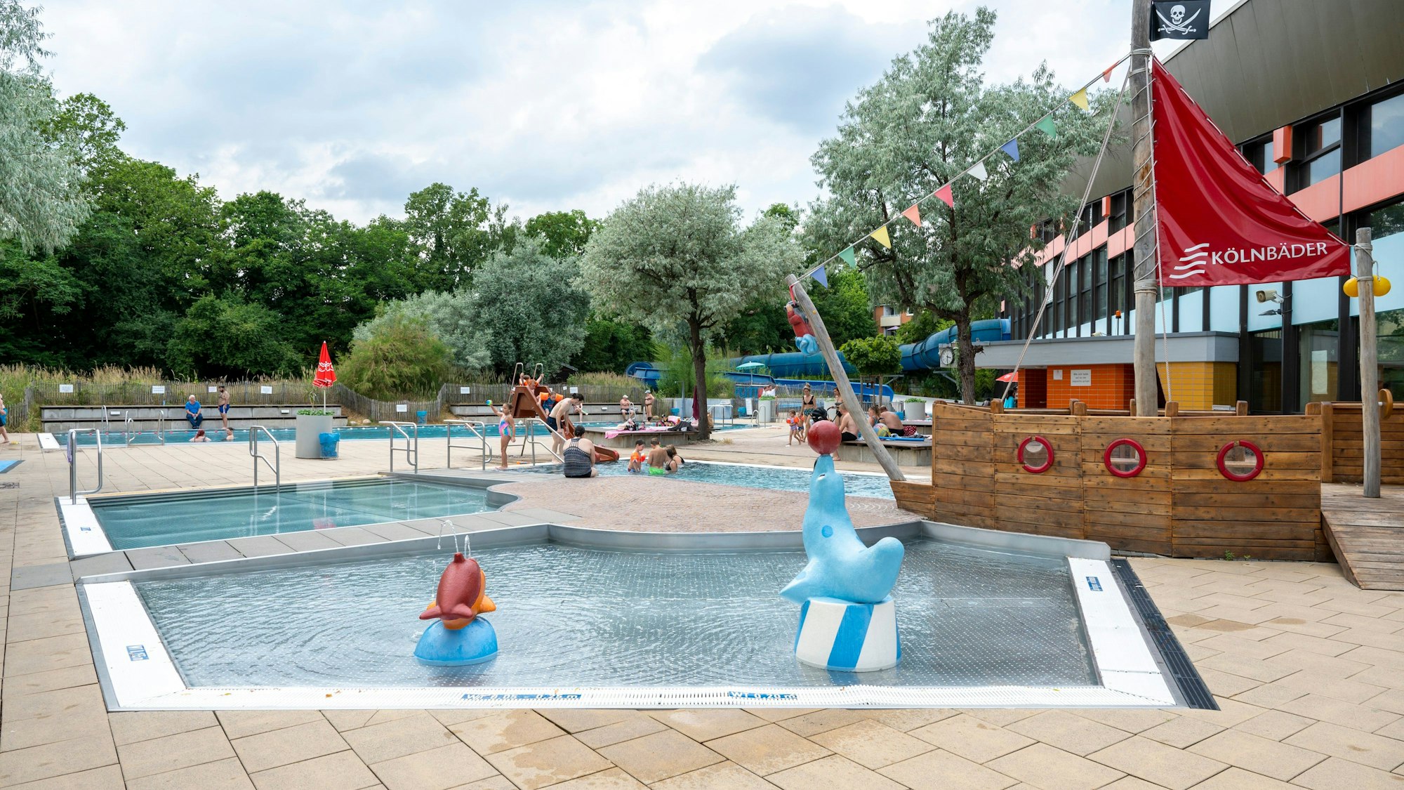 Draußenbecken eines Freibads sind zu sehen, im Vordergrund das Babybecken mit Seehundfiguren und einem Piratenschiff.