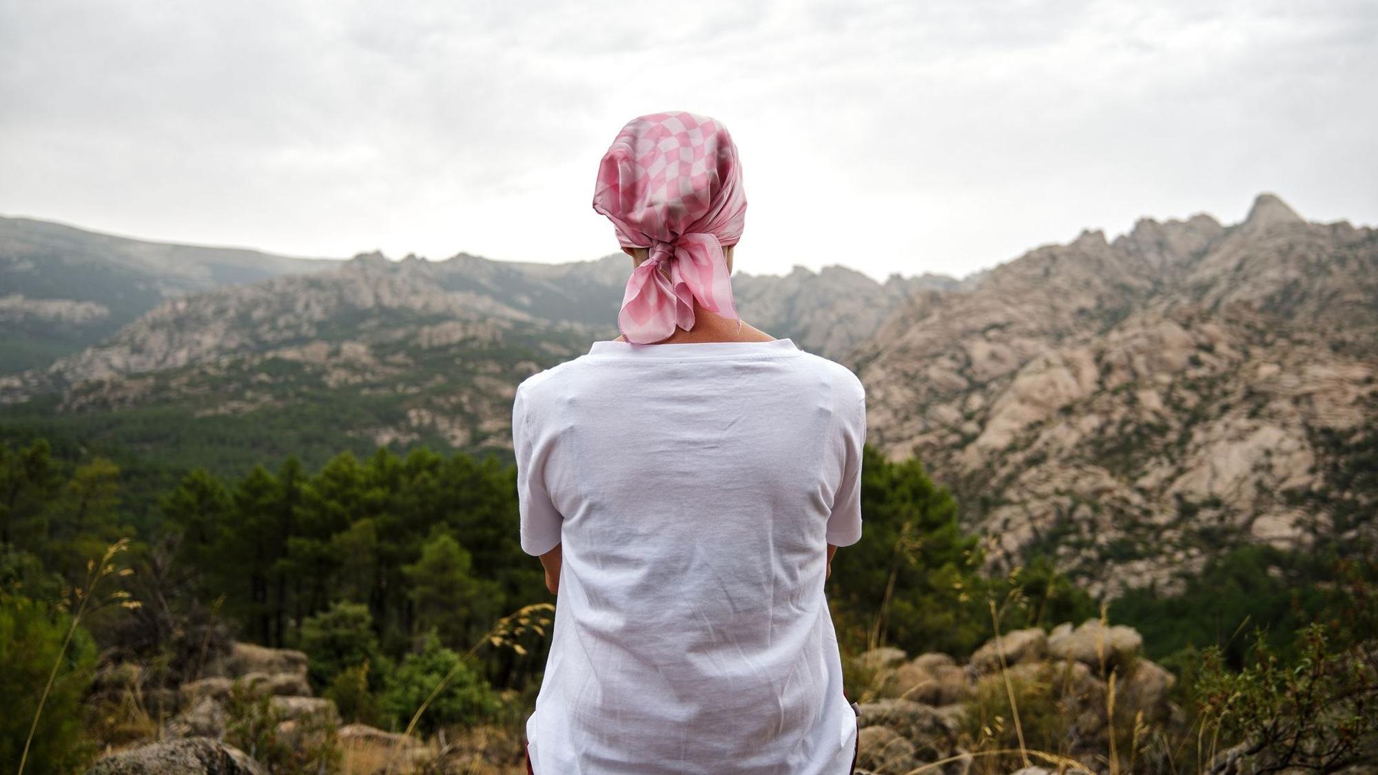 Eine Frau mit Kopftuch sitzt auf einem Berg und schaut in die Landschaft.