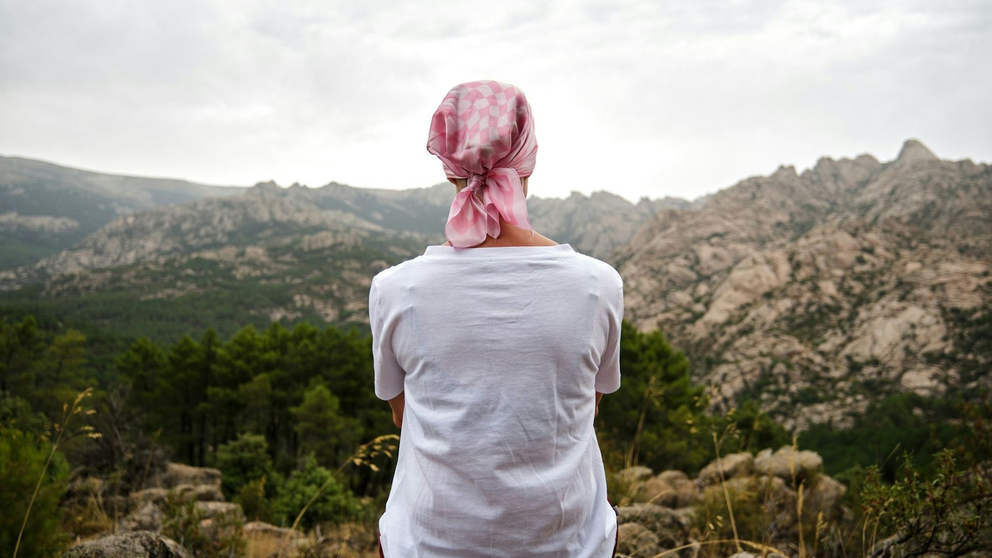 Eine Frau mit Kopftuch sitzt auf einem Berg und schaut in die Landschaft.