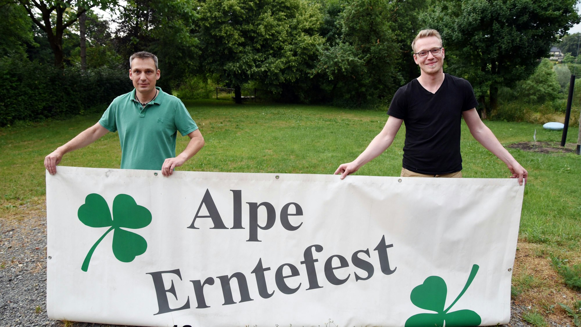 Zwei Männer halten ein großes Plakat in den Händen, auf dem steht: „Alper Erntefest“.