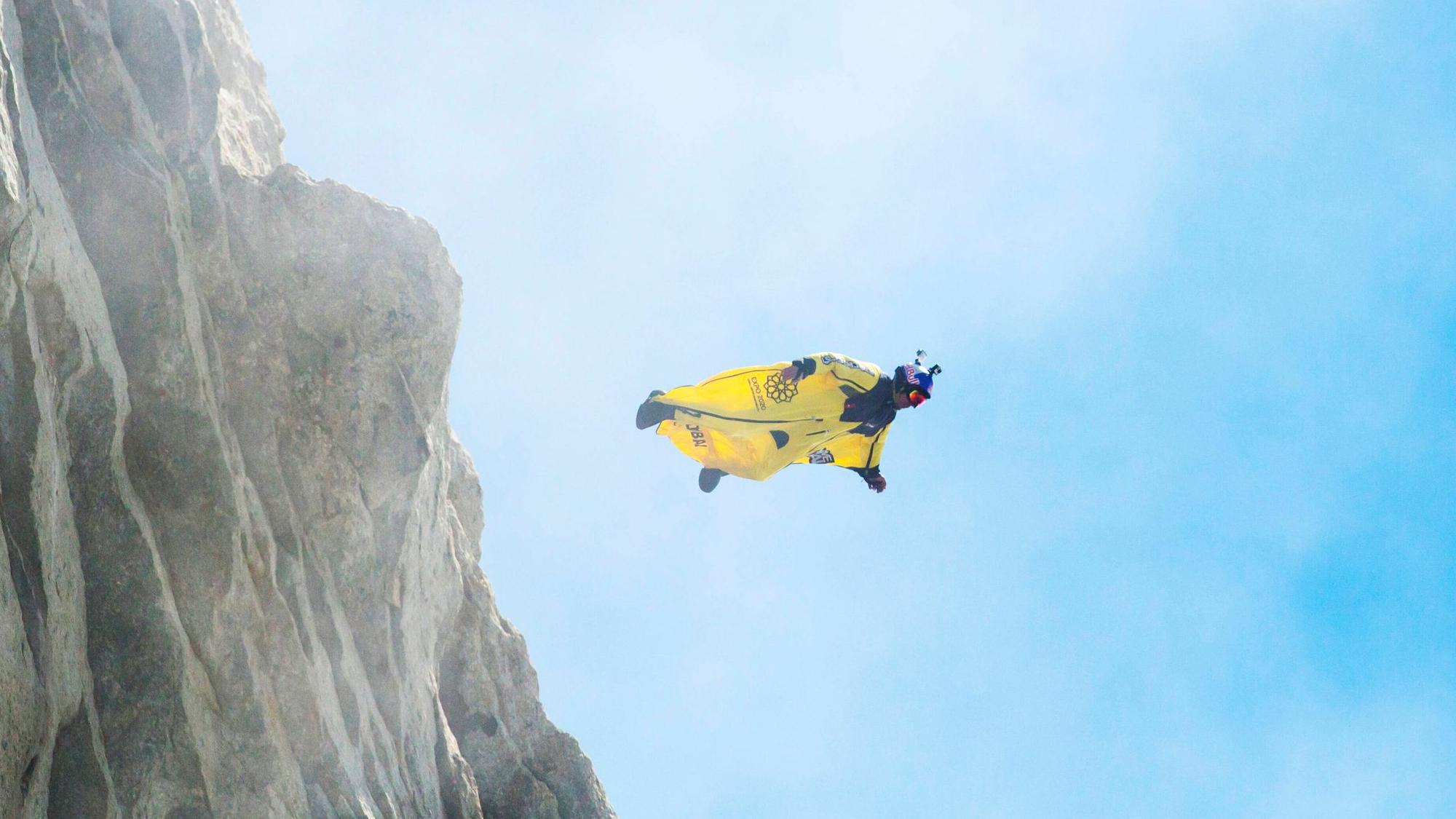 Ein Basejumper in einem gelben Wingsuit springt von einem Felsen (Symbolbild)