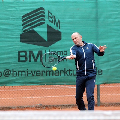 Ein Tennisspieler im Trainingsanzug schlägt einen Ball.