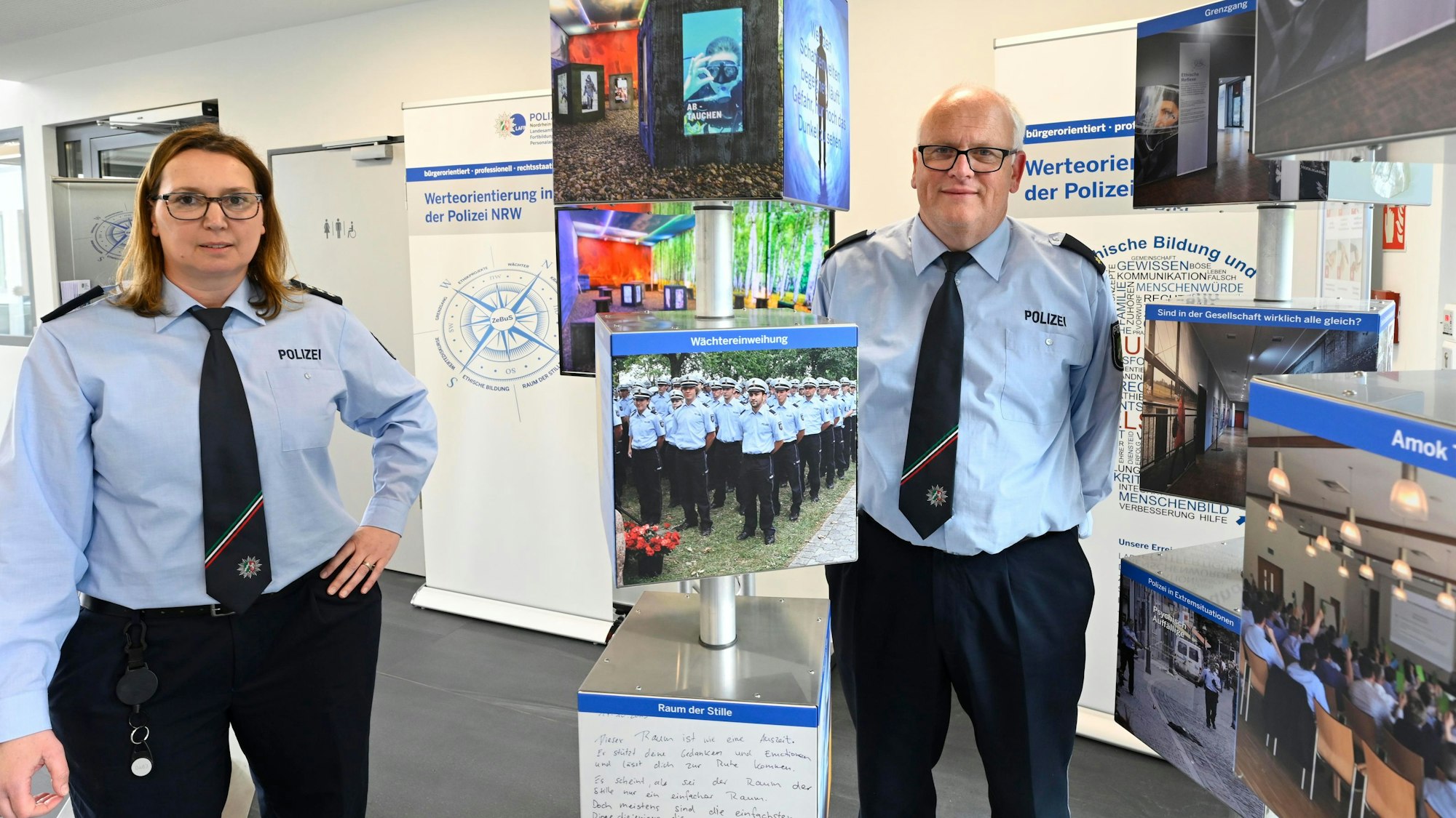 Eine Polizeibeamtin und ihr Kollegen stehen in Uniform zwischen den Tafeln einer Ausstellung.