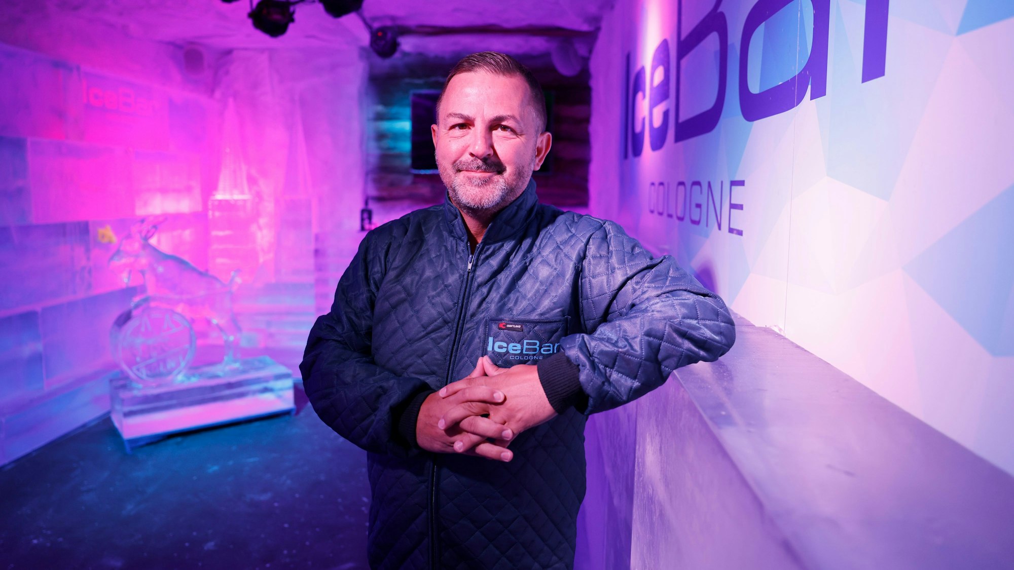 Stefano Straberg steht in seiner Ice Bar in Köln. Im Hintergrund sind der Kölner Dom und Hennes aus Eis zu erahnen.