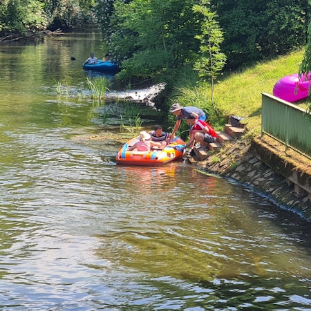 Das Bild zeigt zwei Kinder in einem Schlauchboot auf der Erft. Am Ufer hocken zwei Erwachsene, die das Schlauchboot festhalten.