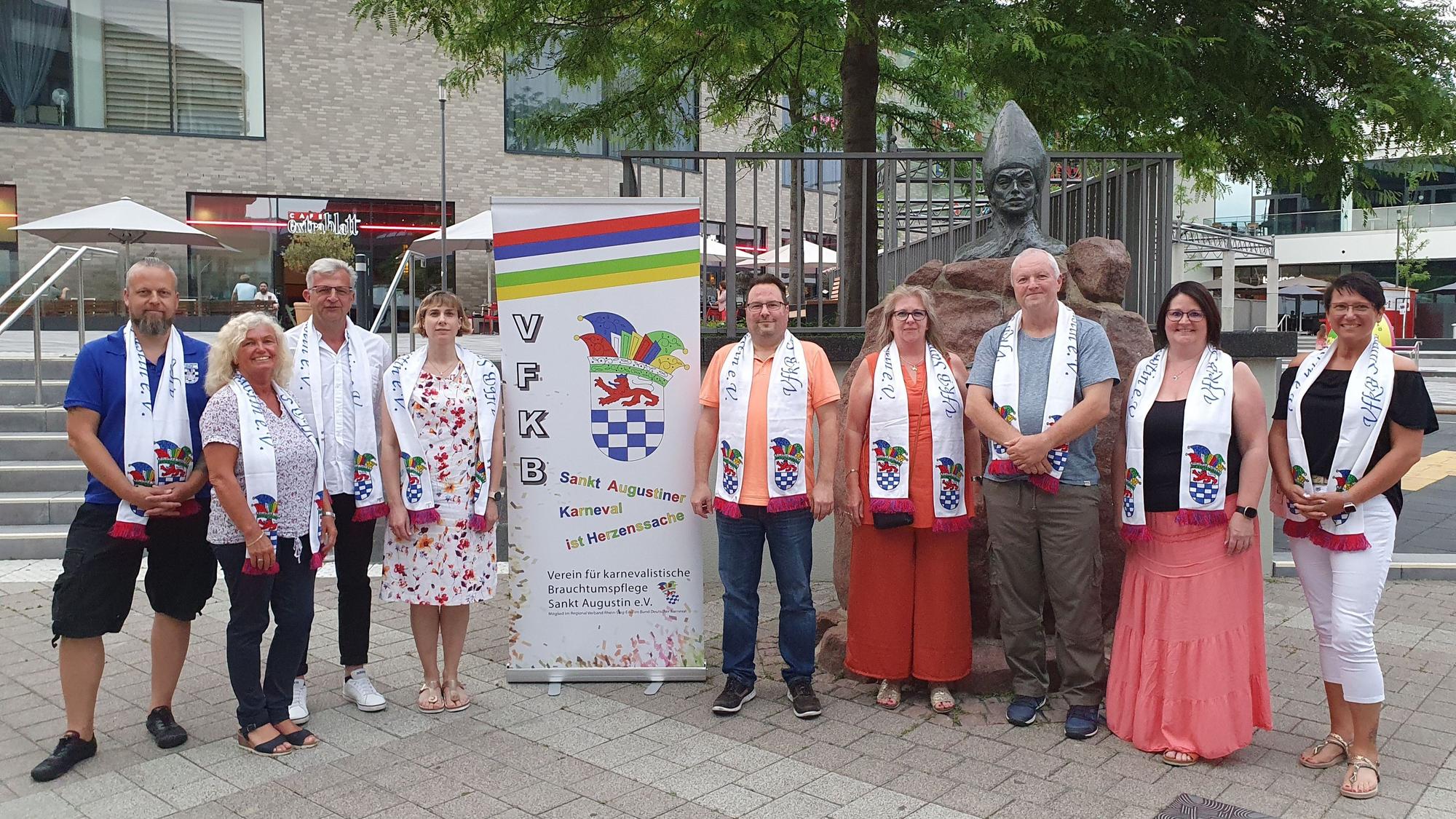 Neben einem Banner stehen die neun Menschen aus dem Vorstand. Sie alle tragen einen weißen Schal des Vereins.