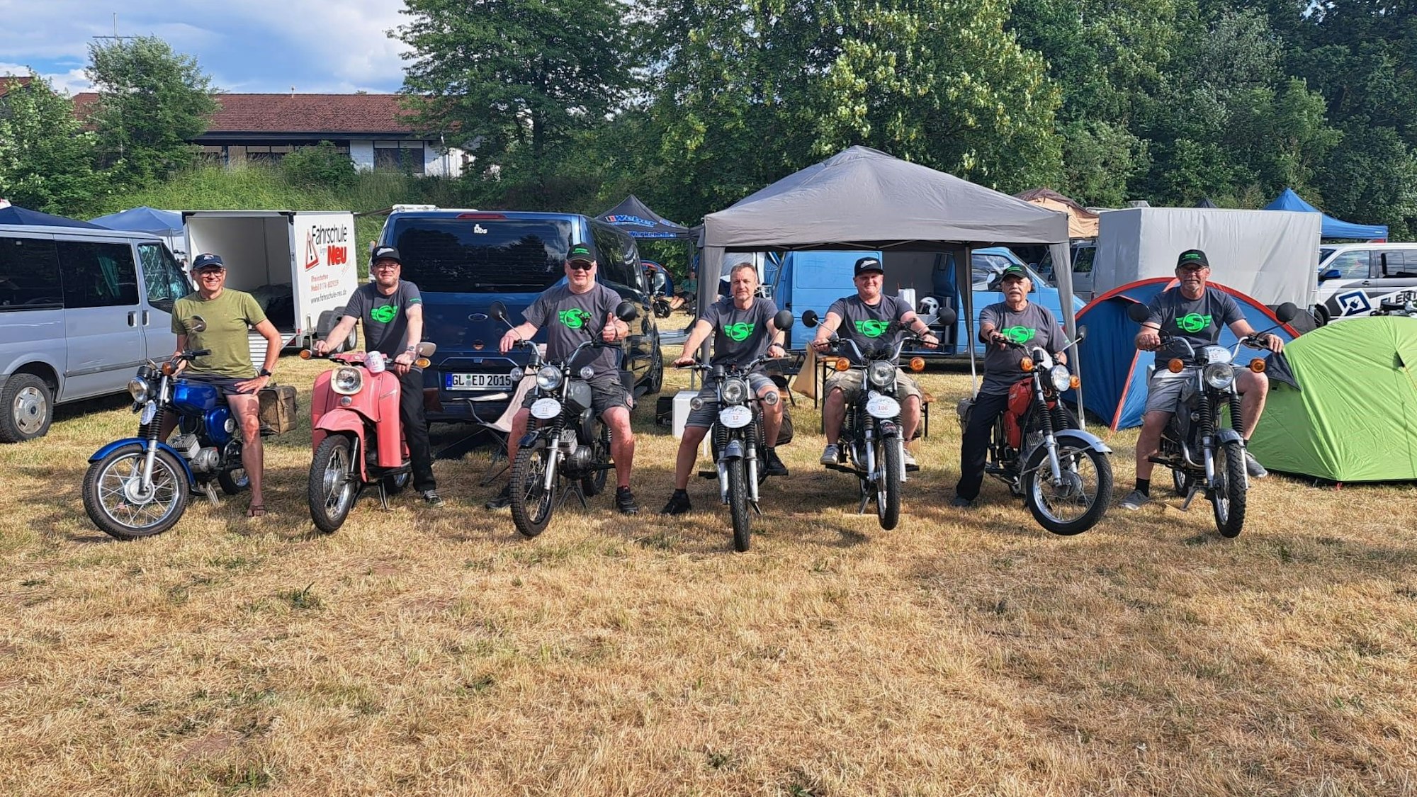 Die Mopedfahrer stehen mit ihren Gefährten nebeneinander.