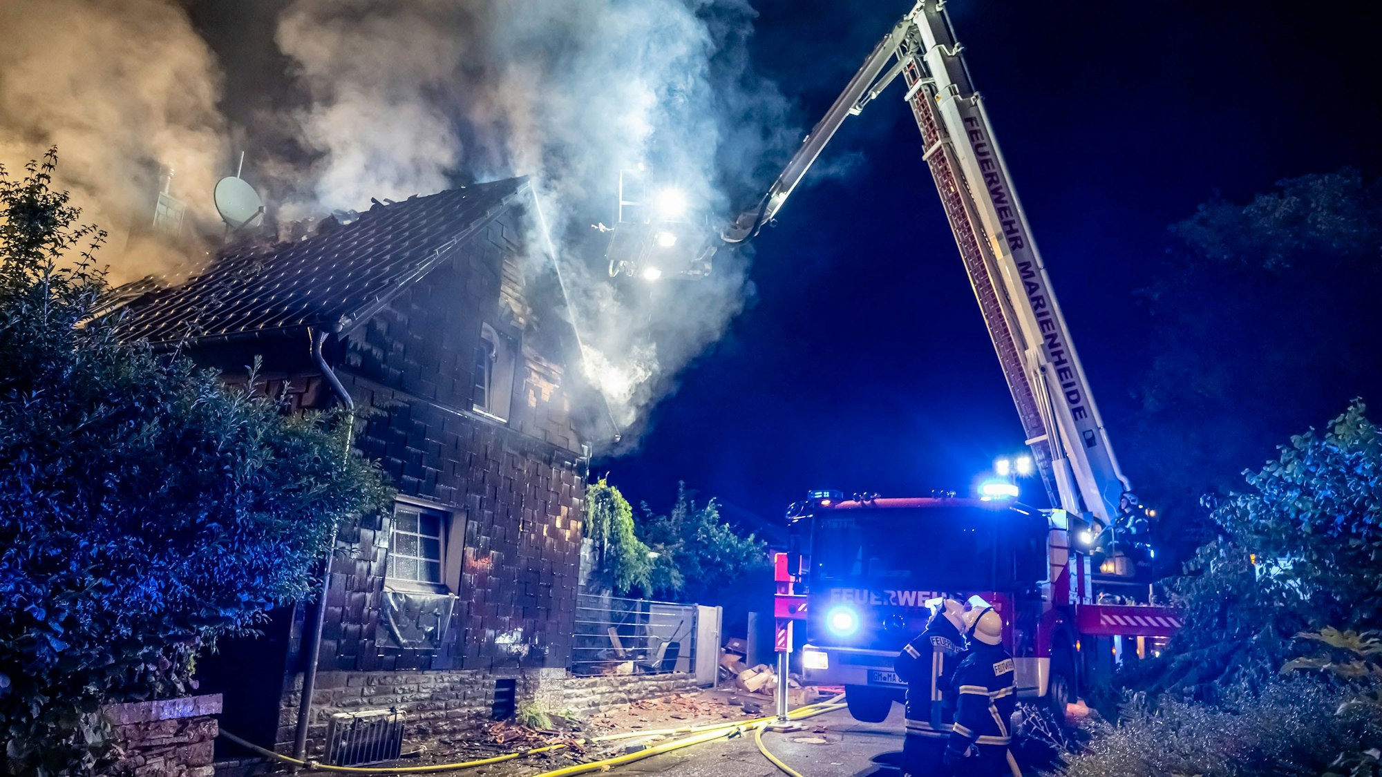Ein Feuerwehrauto steht mit ausgefahrener Drehleiter an einem Haus, aus dem Rauch aufsteigt.