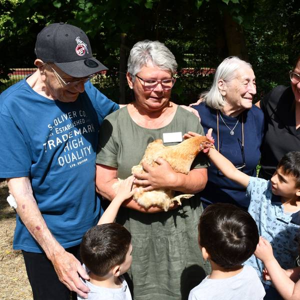 Erwachsene und Kinder begutachten und streicheln ein Huhn im Arm einer Frau.