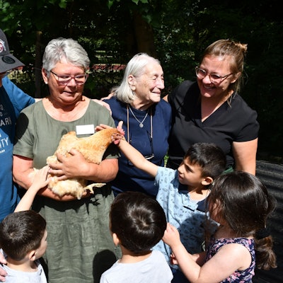 Erwachsene und Kinder begutachten und streicheln ein Huhn im Arm einer Frau.