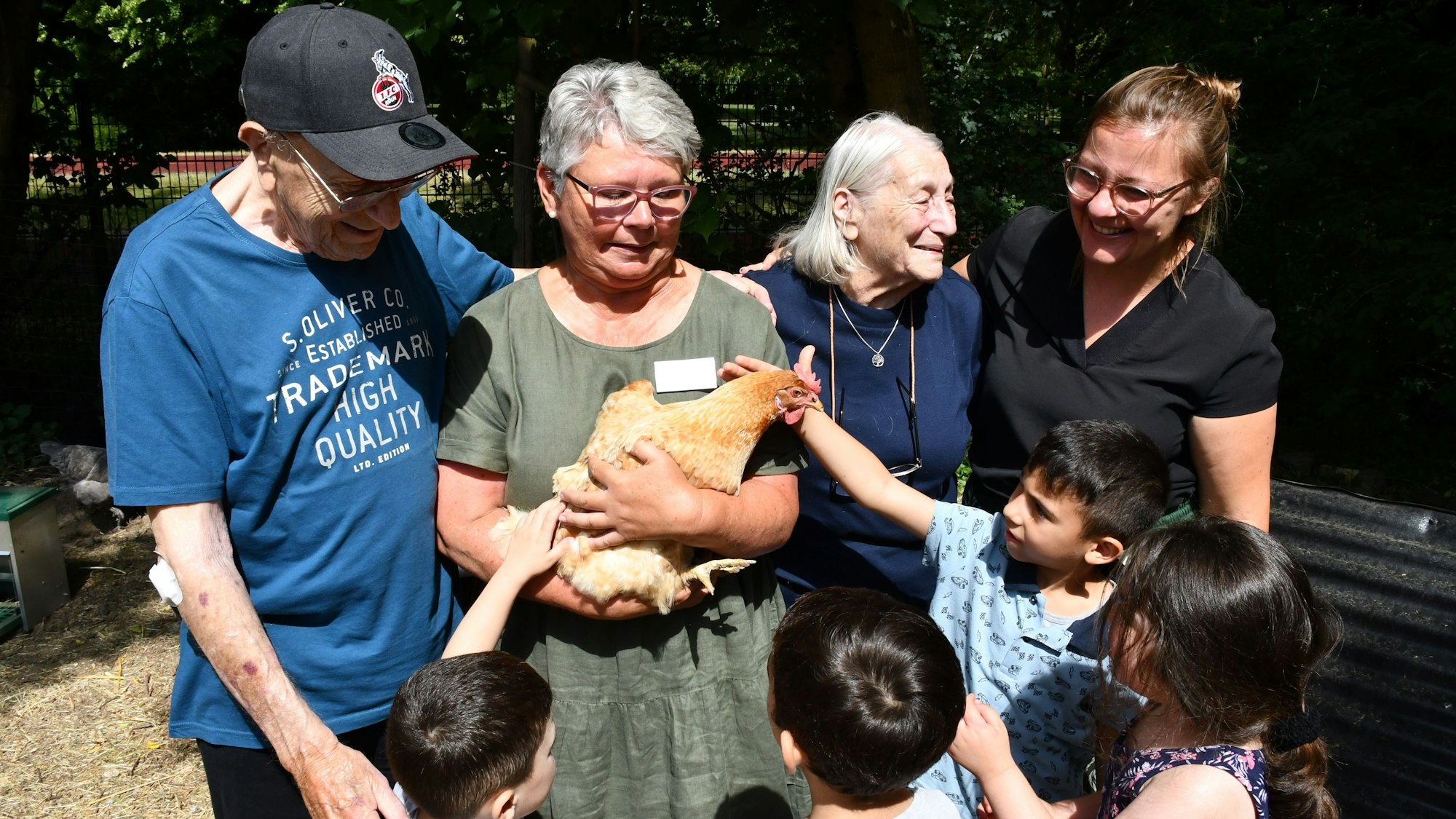Erwachsene und Kinder begutachten und streicheln ein Huhn im Arm einer Frau.