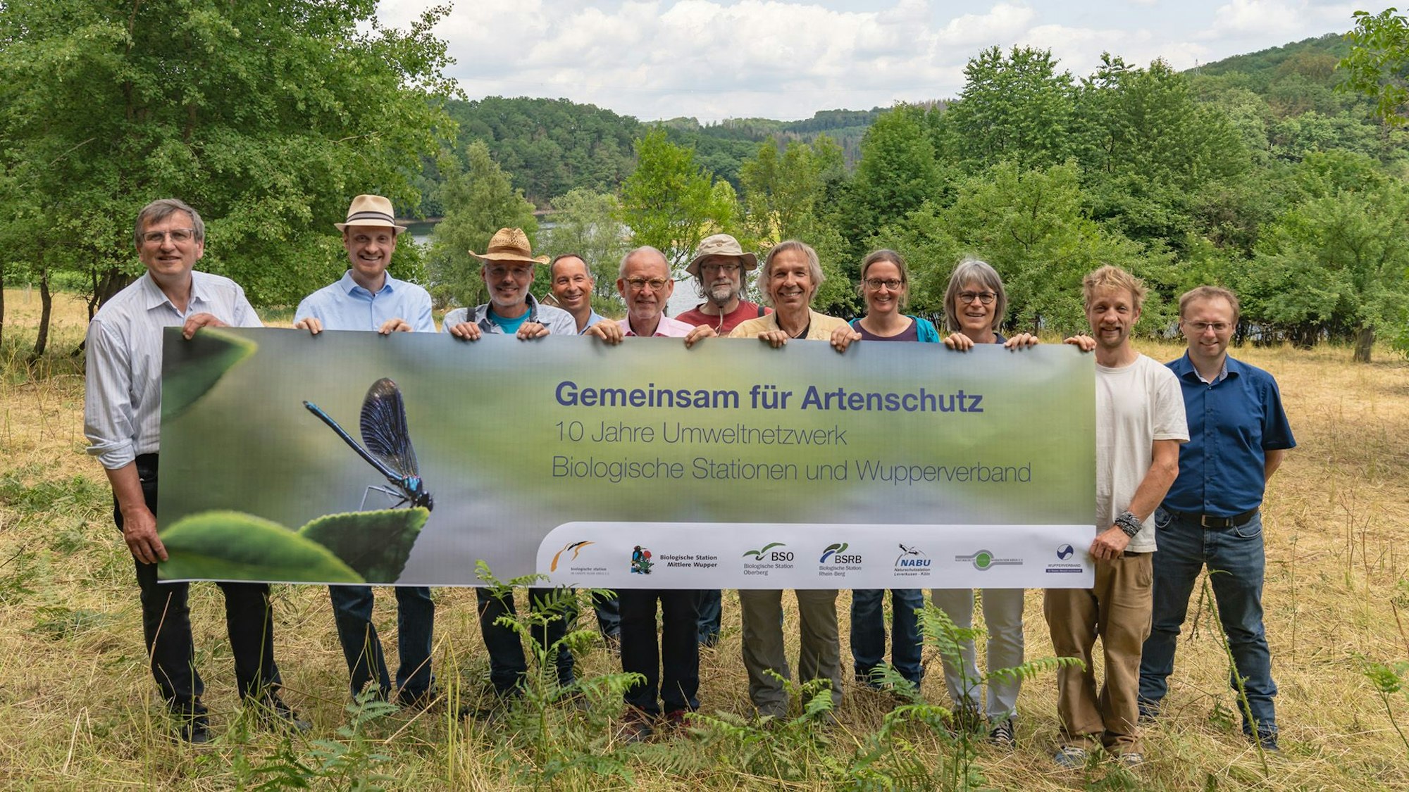 Vertreter der Biologischen Stationen und des Wupperverbandes stehen auf einer Wiese und halten ein Transparent für den Artenschutz in die Luft.
