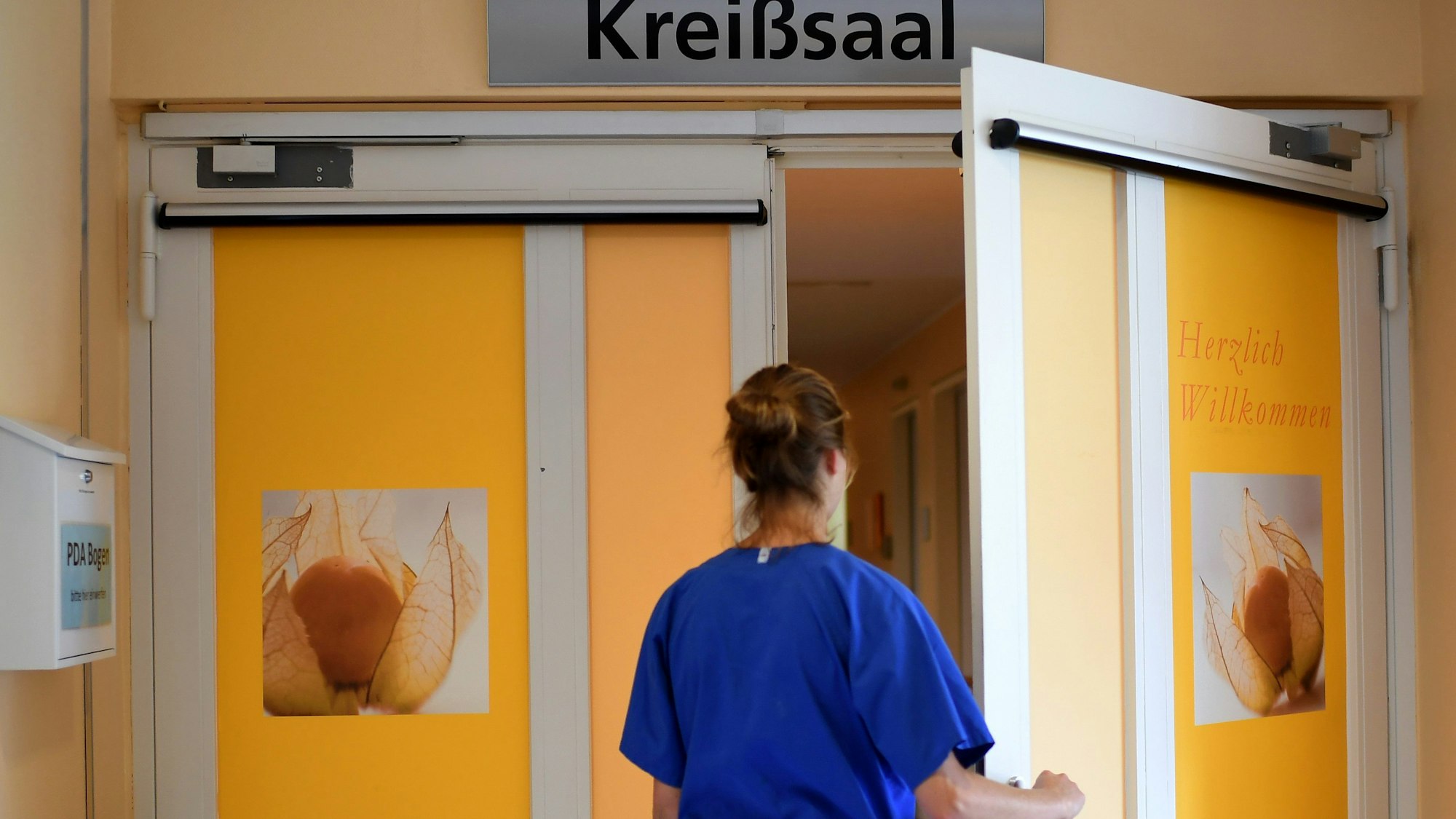 Eine Mitarbeiterin steht vor einem Kreißsaal in einem Krankenhaus