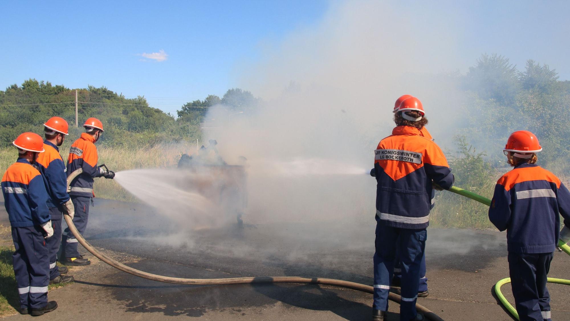 Mehrere Feuerwehrleute hantieren mit Schläuchen und löschen einen Schaubrand.
