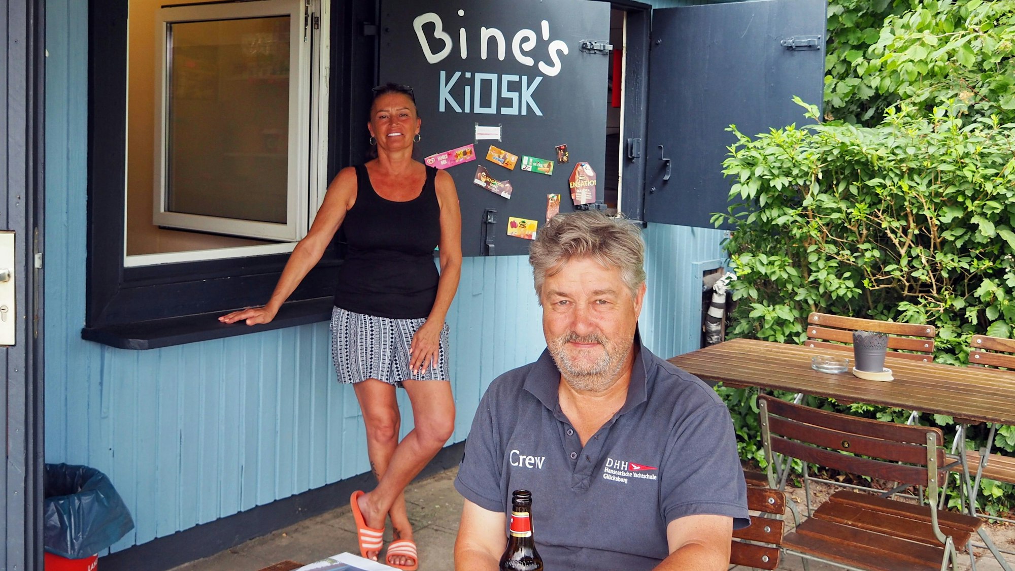 Kiosk mit Holzverkleidung, Jansen steht am Tresen, Thelen sitzt an einem Holztisch