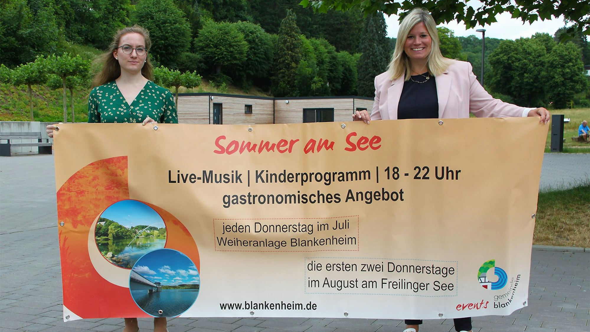 Zwei Frauen halten ein großes Veranstaltungs-Transparent in die Höhe.