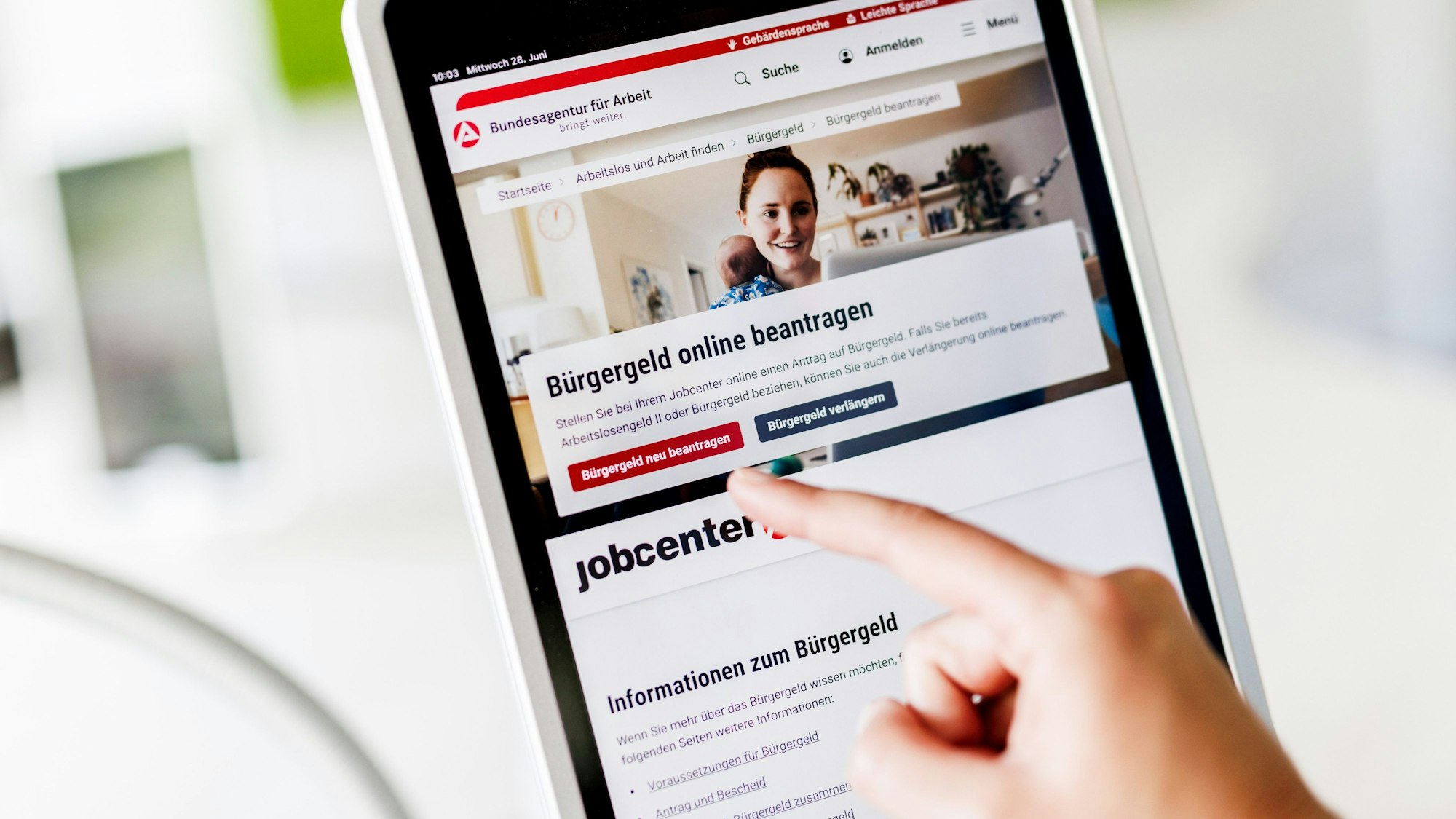 Eine Frau tippt auf einem Tablet auf einen Link zum Beantragen des Bürgergeldes im Kundenbereich im Jobcenter Berlin Mitte.